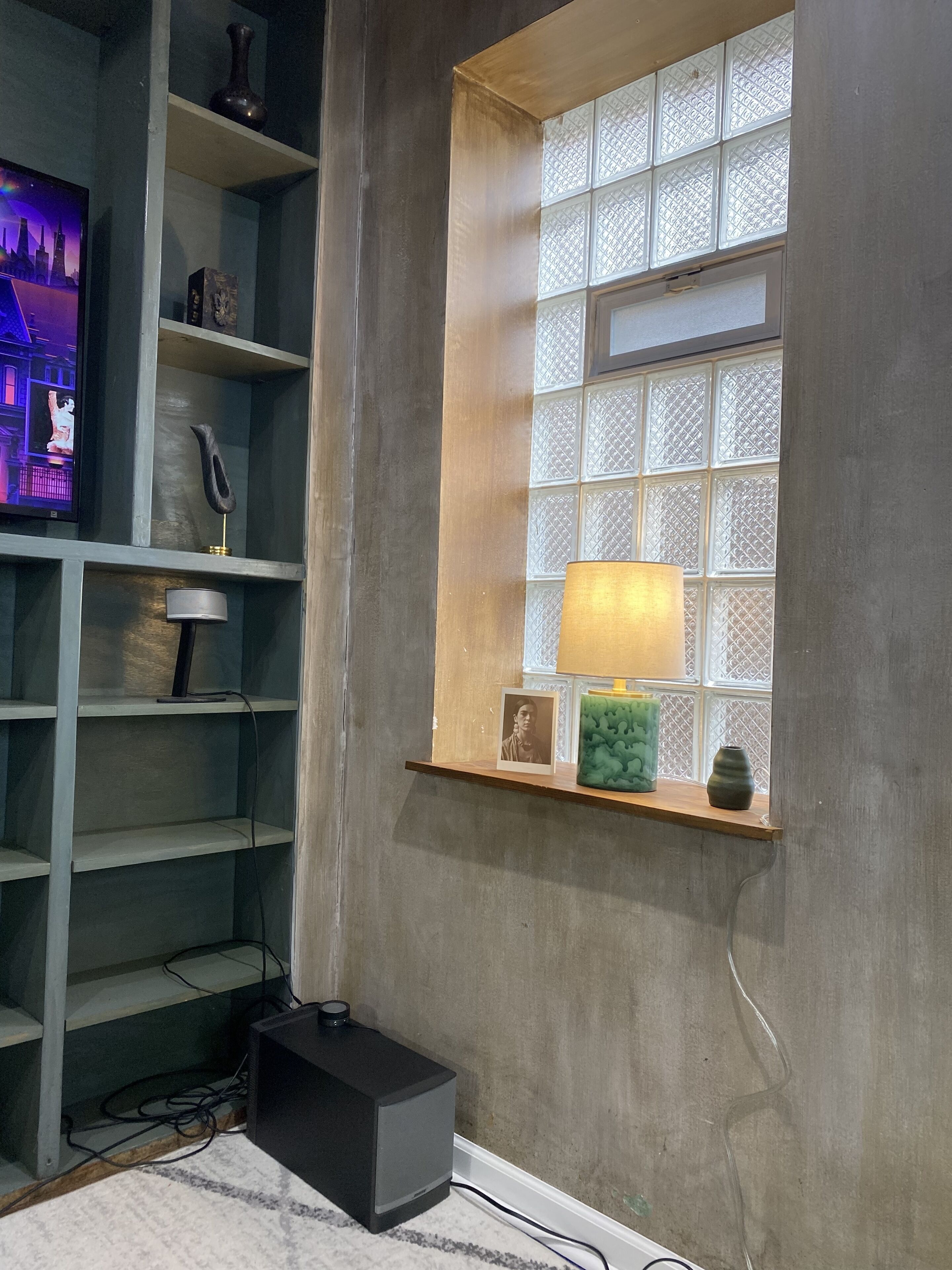 A room with a built-in shelf, a window with decorative glass, a lamp, and a television on a stand.