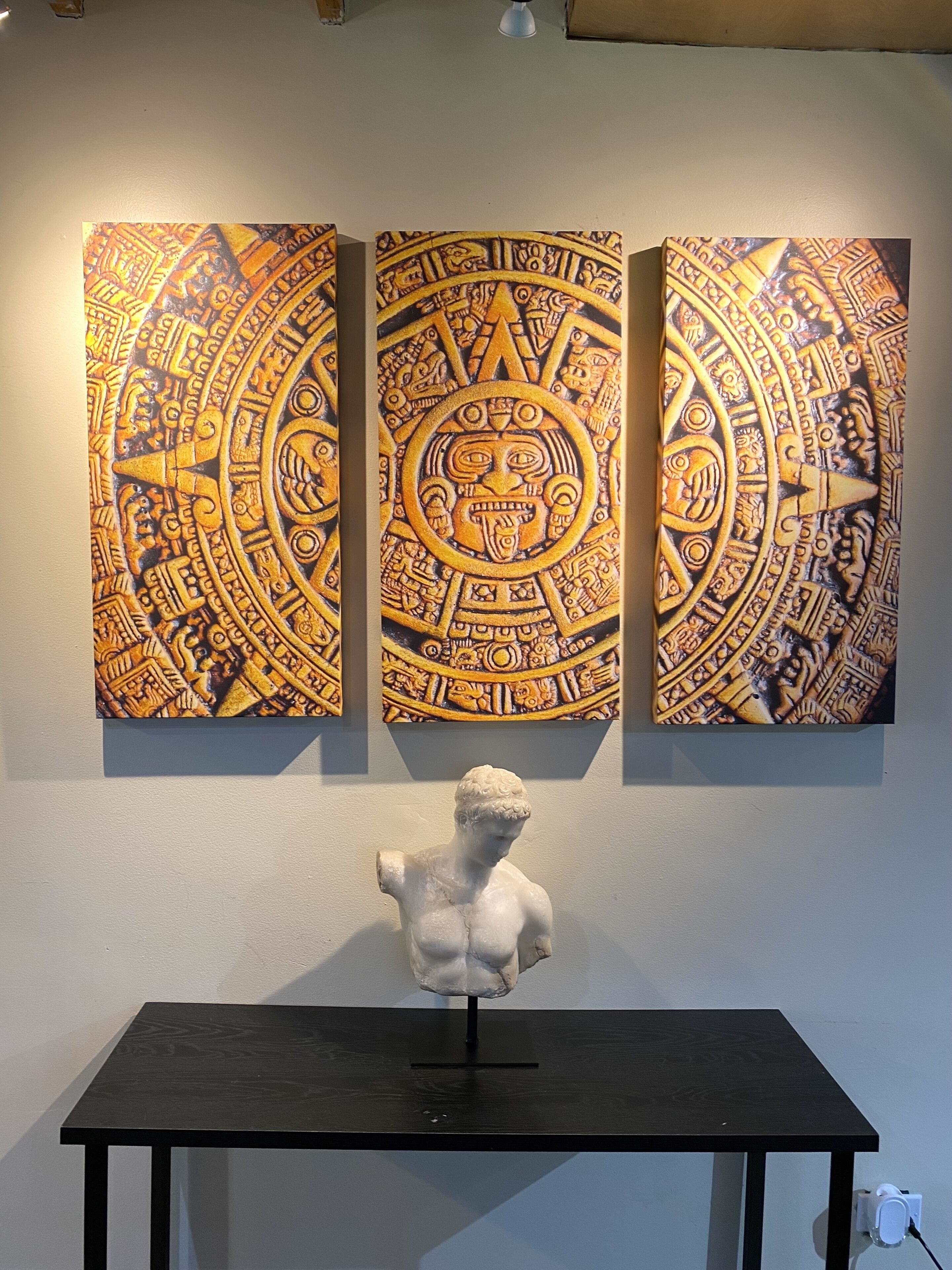Una pared con tres paneles de obra artística intrincada y una escultura de busto sobre una mesa.