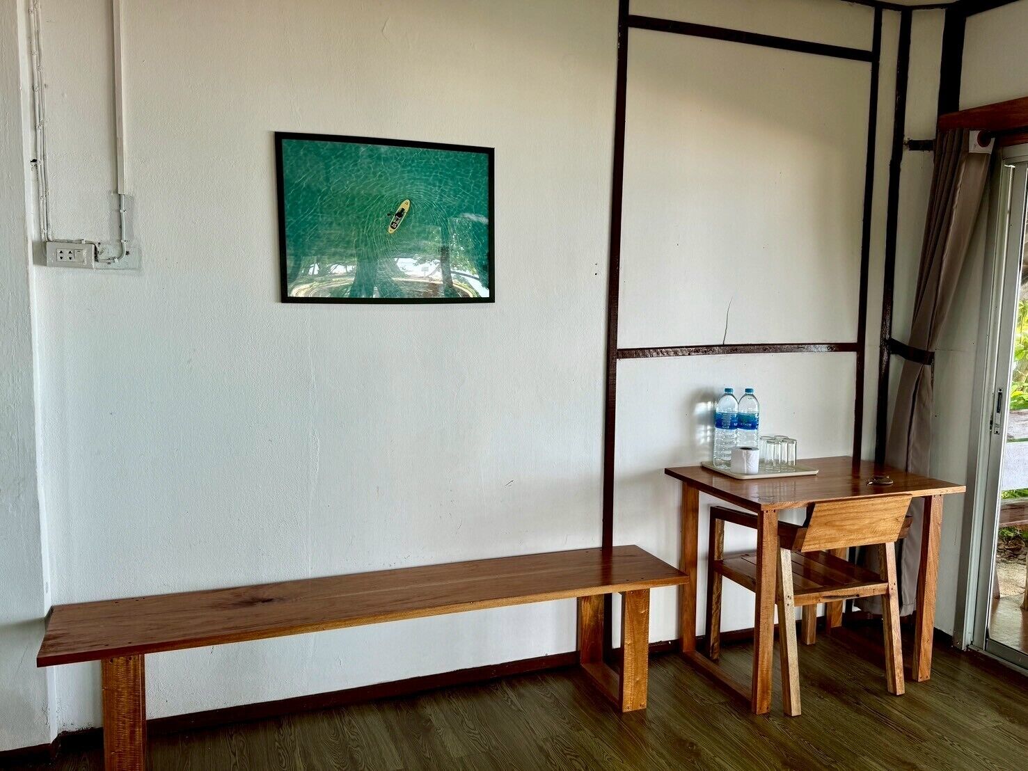A wooden bench and table in a room with a white wall and a framed picture.