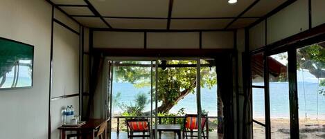 A room with a view of the sea, a bench, a table, and two chairs.