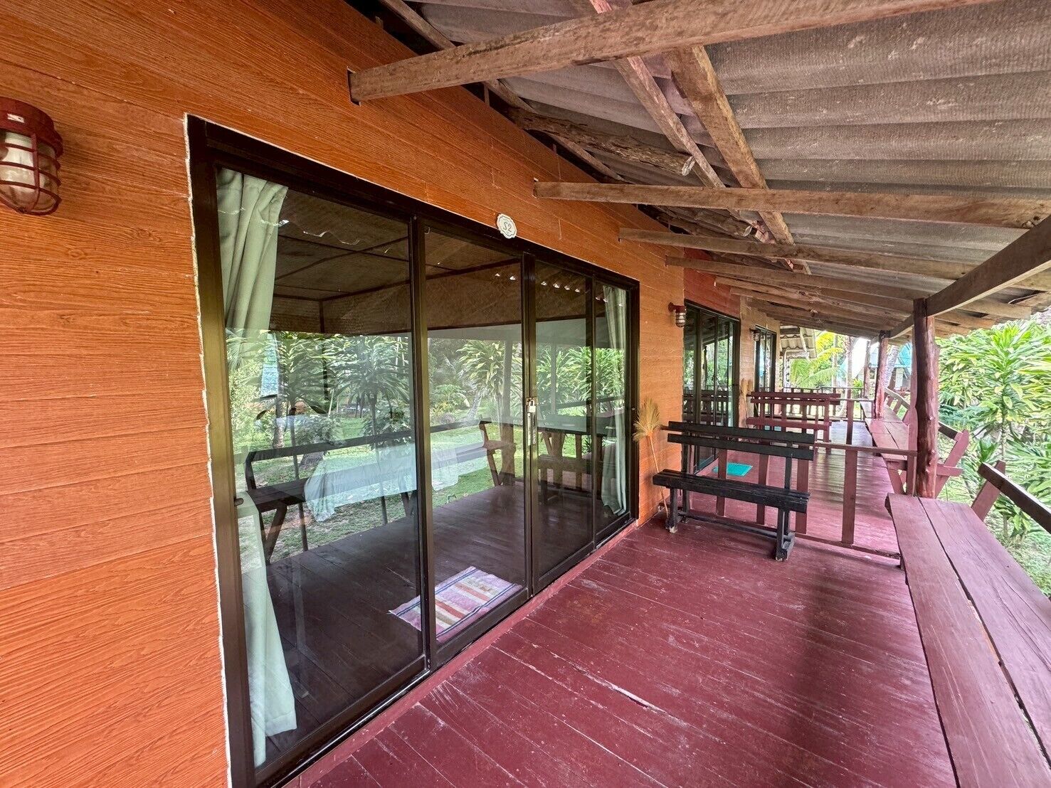 A covered outdoor seating area with wooden benches and a glass door leading to a lush garden.