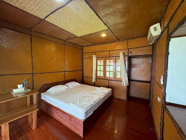 A wooden room with a bed, a small table, and a window with curtains.