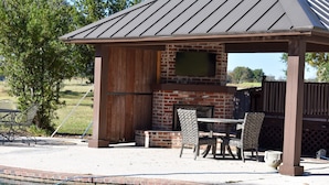 A covered outdoor barbecue area with a brick oven, seating, and a pool. - Youngsville Retreat- pool, private pond, outdoor fireplace  (Broussard)