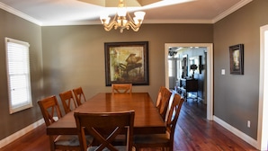 A dining room with a large wooden table and chairs, a chandelier, and a framed painting on the wall. - Youngsville Retreat- pool, private pond, outdoor fireplace  (Broussard)