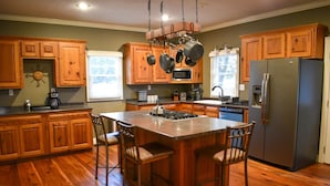 A kitchen with wooden cabinets, a stainless steel refrigerator, and a central island with bar stools. - Youngsville Retreat- pool, private pond, outdoor fireplace  (Broussard)