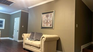 Un soggiorno con un divano color beige, un quadro appeso al muro e una porta sullo sfondo.