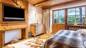 A wooden room with a fireplace, a television, a bed, and a window with a view of mountains.