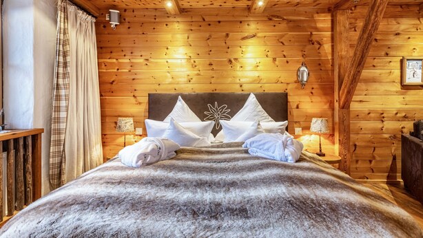 A wooden-paneled room with a bed, pillows, a lamp, and a wall-mounted light fixture.