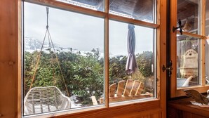 A wooden-framed window with a view of a snowy mountain and greenery.