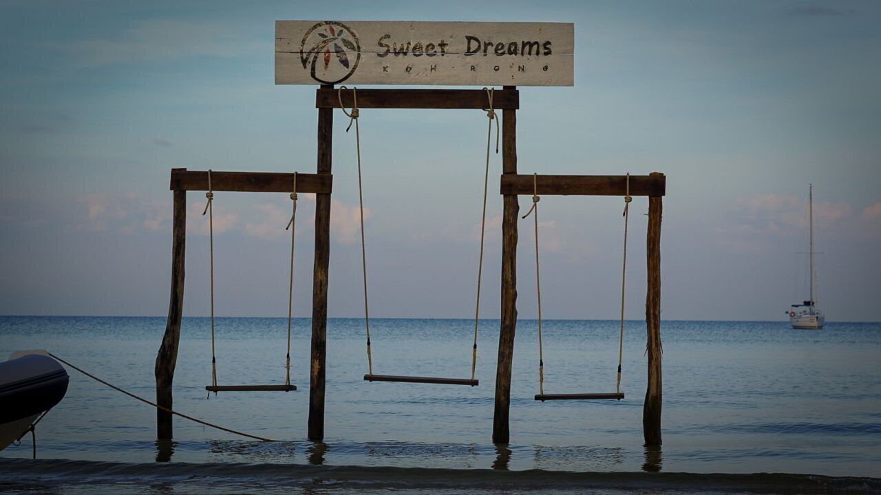 A wooden swing set with a sign reading "Sweet Dreams Koh Rong" by the sea.