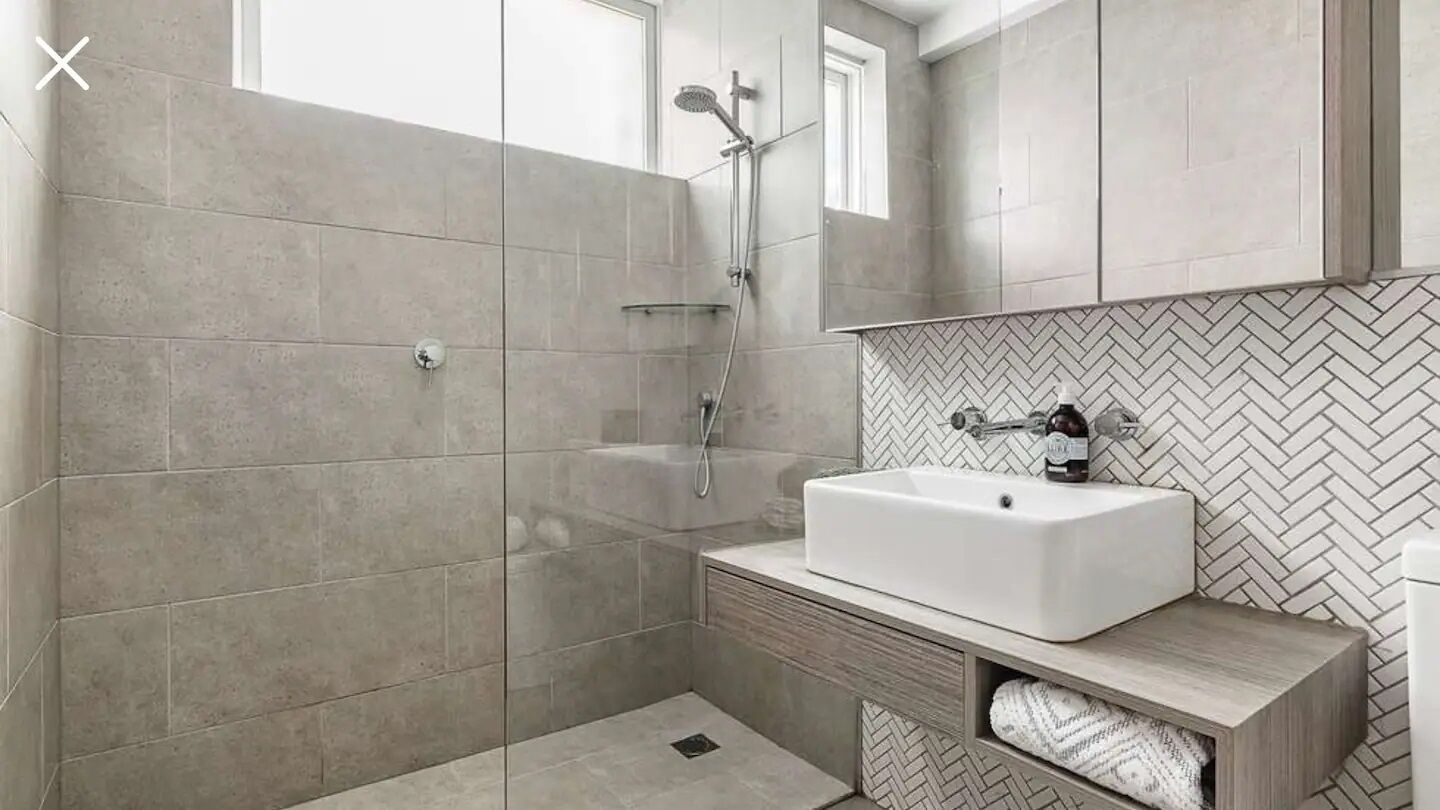 Une salle de bain moderne avec une douche à parois de verre, un lavabo blanc et un pare-feu en mosaïque disposée en motif chevrons.