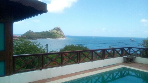 Un balcon avec une piscine, offrant une vue sur la côte, une petite île et la mer.