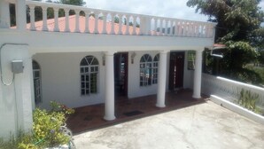 Un bâtiment blanc doté d’un patio couvert, de colonnes et d’un toit recouvert de tuiles rouges.