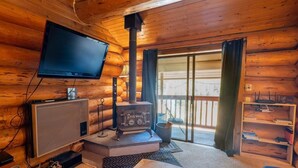 Ein Blockhaus-Interieur mit Fernseher, Holzofen und einer Schiebetür nach draußen.