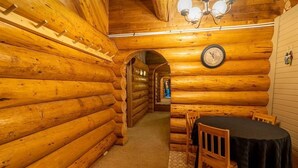 Ein Holzblockhaus-Interieur mit Essbereich, inklusive Tisch und Stühlen, einer Wanduhr und einer Treppe, die zu einem anderen Raum führt.