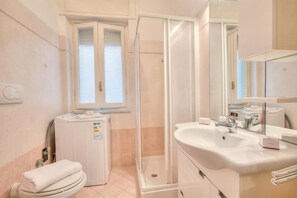 Een badkamer met toilet, douchecabine, wastafel en spiegel.