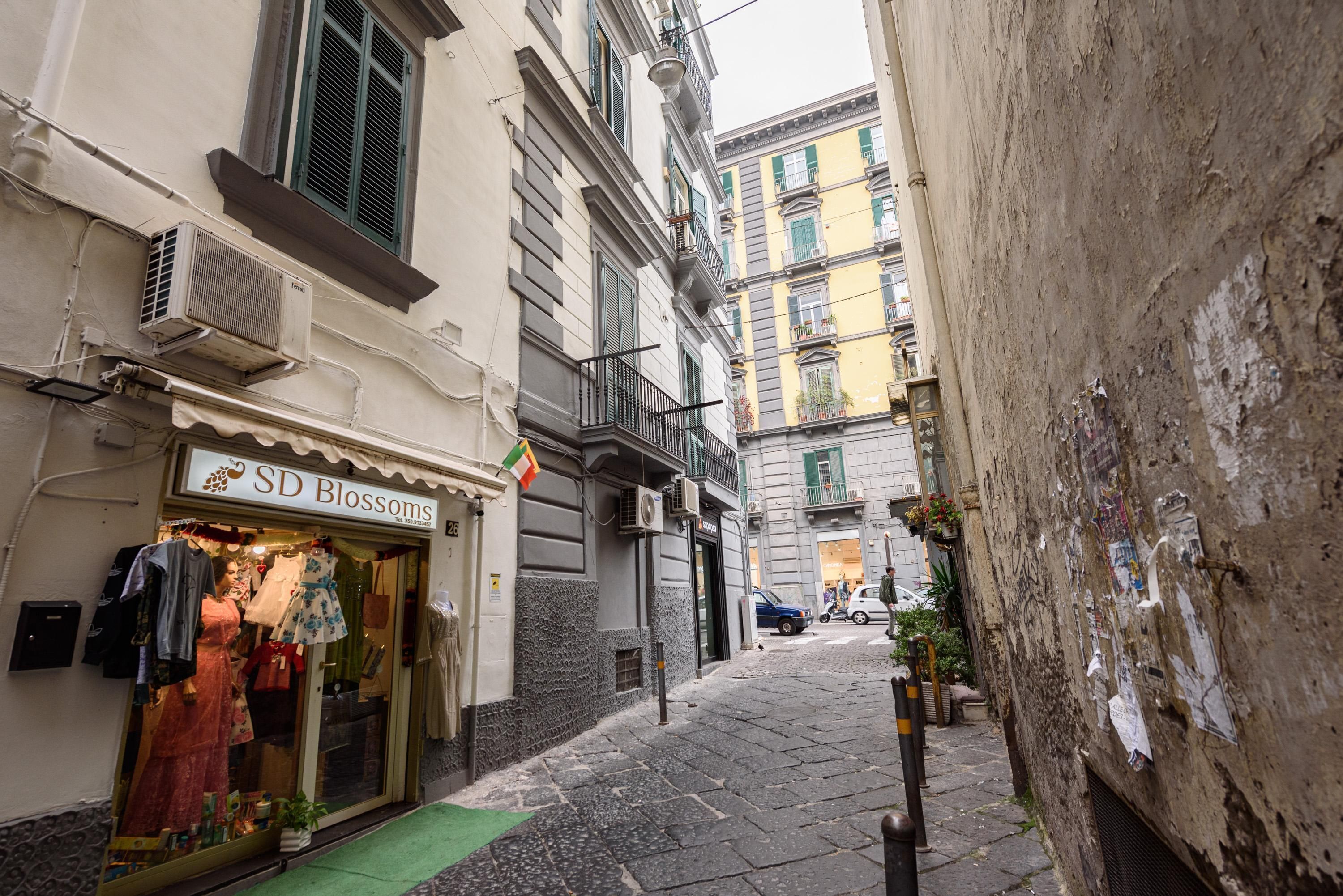 A narrow street with a boutique store named 'SD Blossoms' on the left, featuring mannequins displaying clothing.