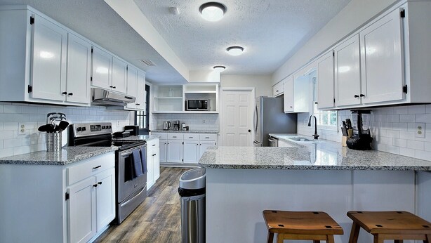 A modern kitchen with white cabinets, granite countertops, stainless steel appliances, and wooden stools. - 5BR, 3BA Spacious N. Columbus Villa w/Hot Tub, BBQ, Play Area, 13 mi. to Benning (Columbus)