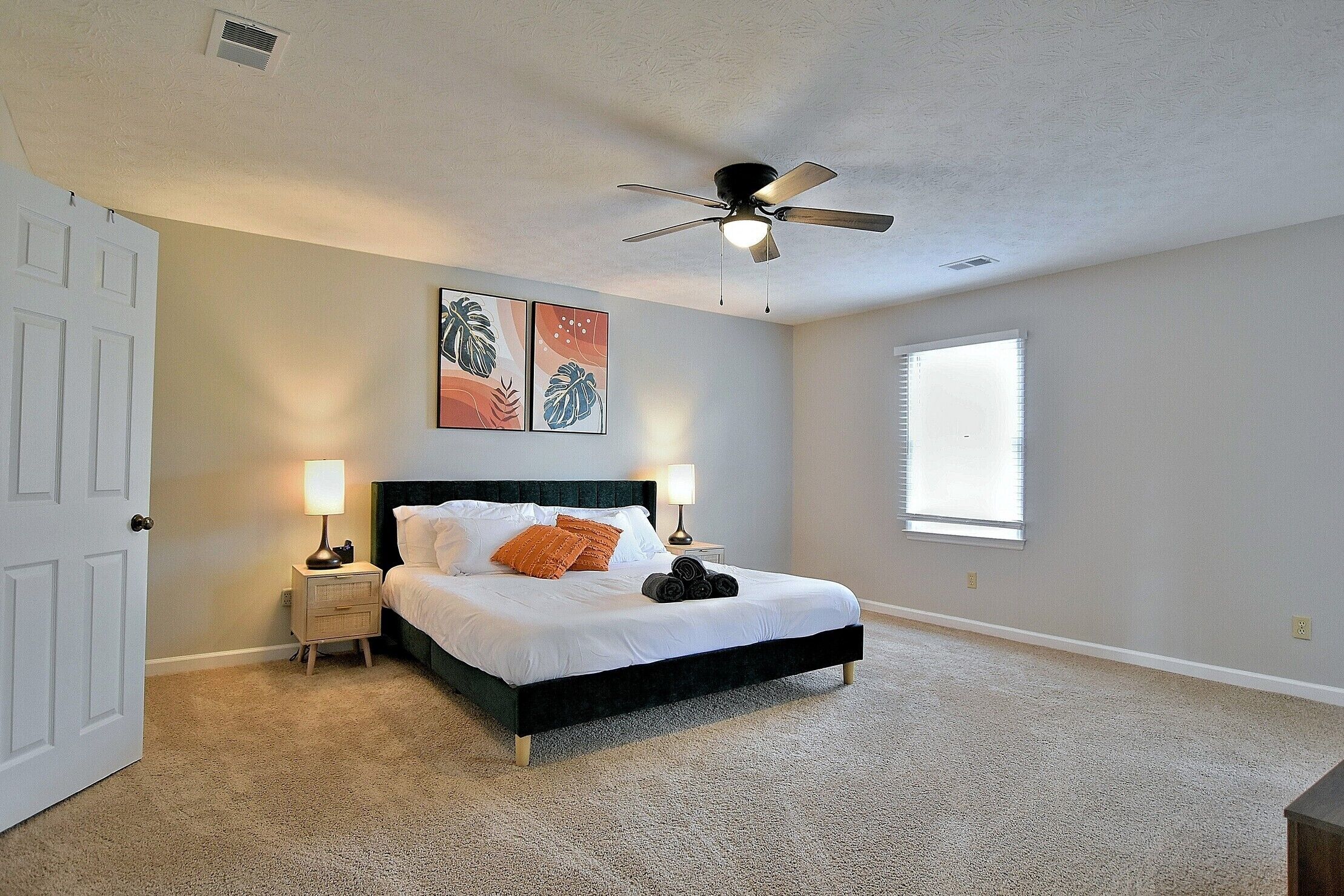 A bedroom with a bed, two bedside tables, a ceiling fan, and a window.