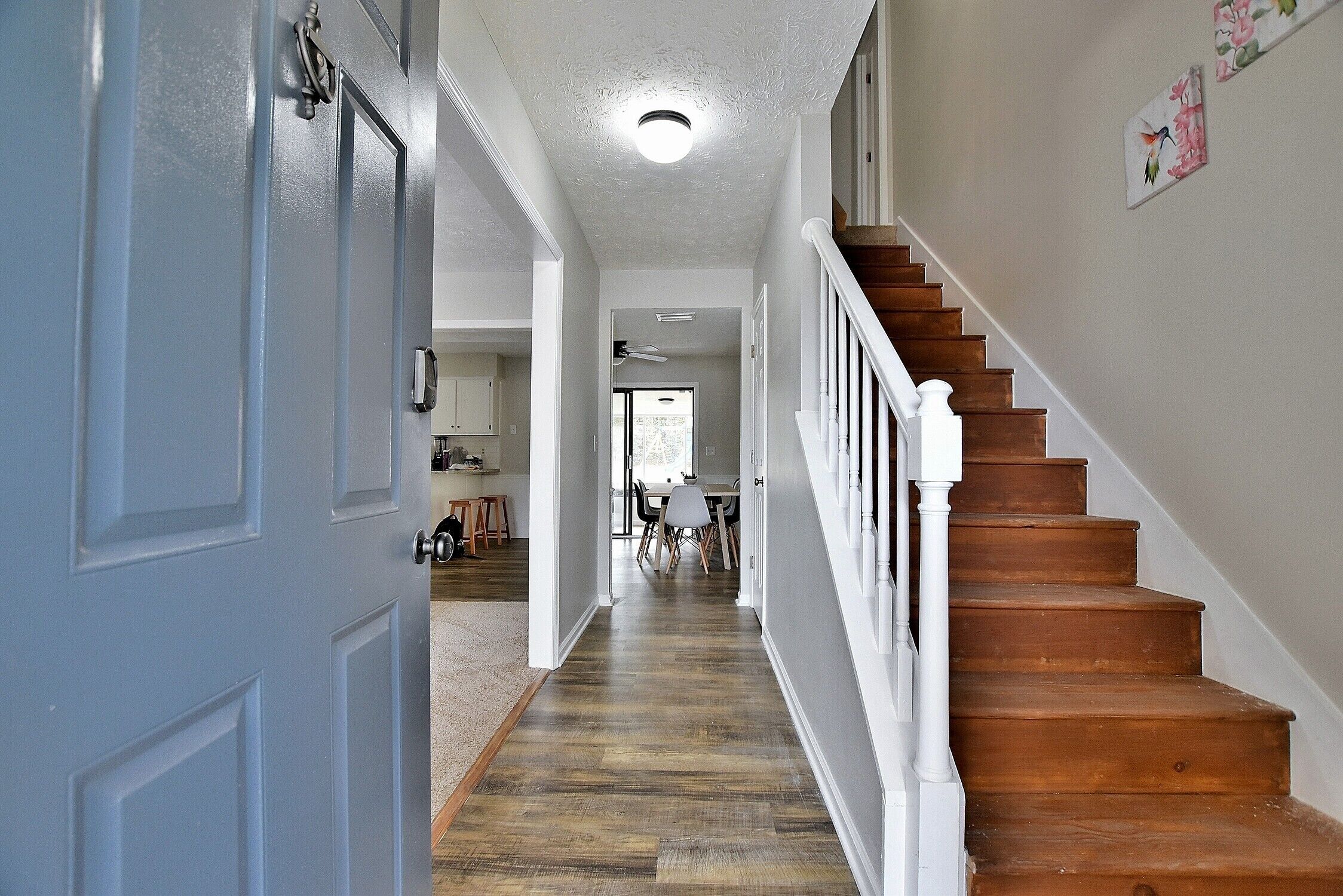 A hallway with a wooden staircase, a white door, and a ceiling fan.