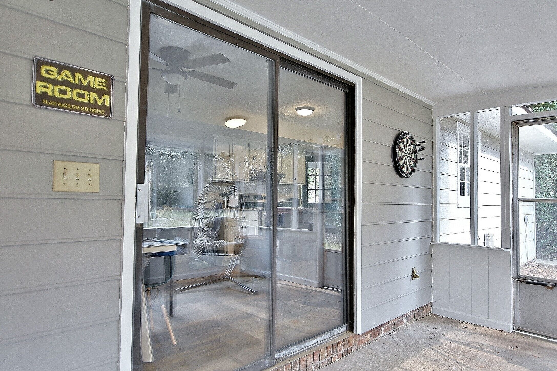 A room with a sliding glass door leading to a patio area, a ceiling fan, and a dartboard on the wall.