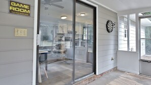 A room with a sliding glass door leading to a patio area, a ceiling fan, and a dartboard on the wall. - 5BR, 3BA Spacious N. Columbus Villa w/Hot Tub, BBQ, Play Area, 13 mi. to Benning (Columbus)