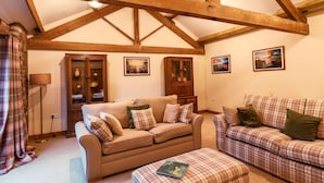 A cozy living room with a high wooden ceiling, two sofas with plaid cushions, a wooden cabinet, and framed pictures on the wall.