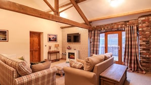 A cozy living room with a fireplace, wooden beams, and plaid furniture.