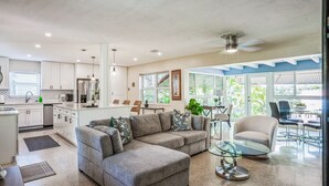 A spacious living area with a grey sectional sofa, a glass coffee table, and a dining area with a glass table and chairs.