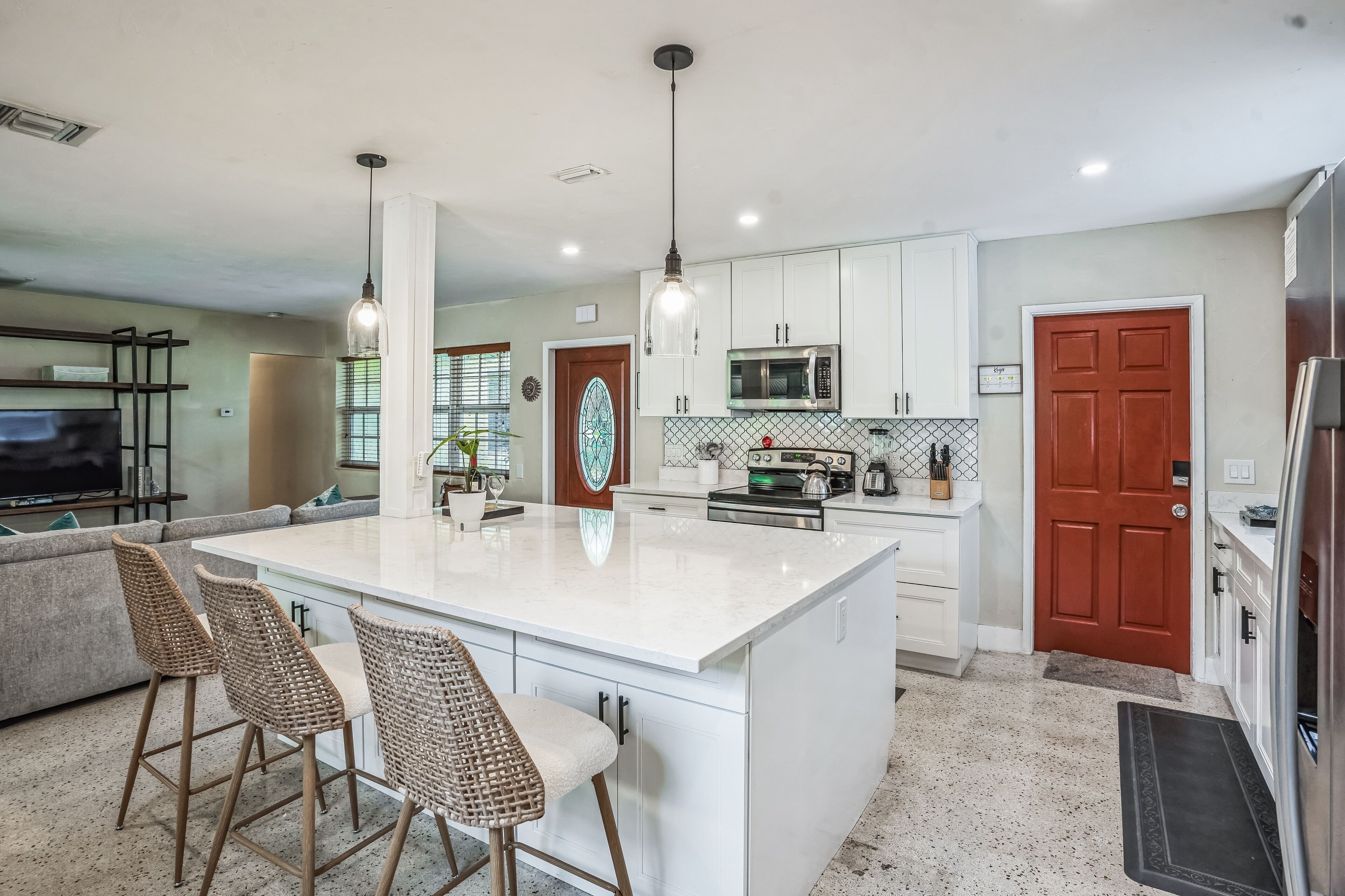 A modern kitchen with white cabinets, a large island with bar stools, stainless steel appliances, and pendant lighting.