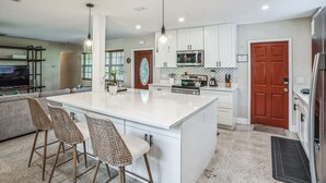 A modern kitchen with white cabinets, a large island with bar stools, stainless steel appliances, and pendant lighting.