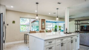 A spacious kitchen with a large island, white cabinetry, and pendant lighting.