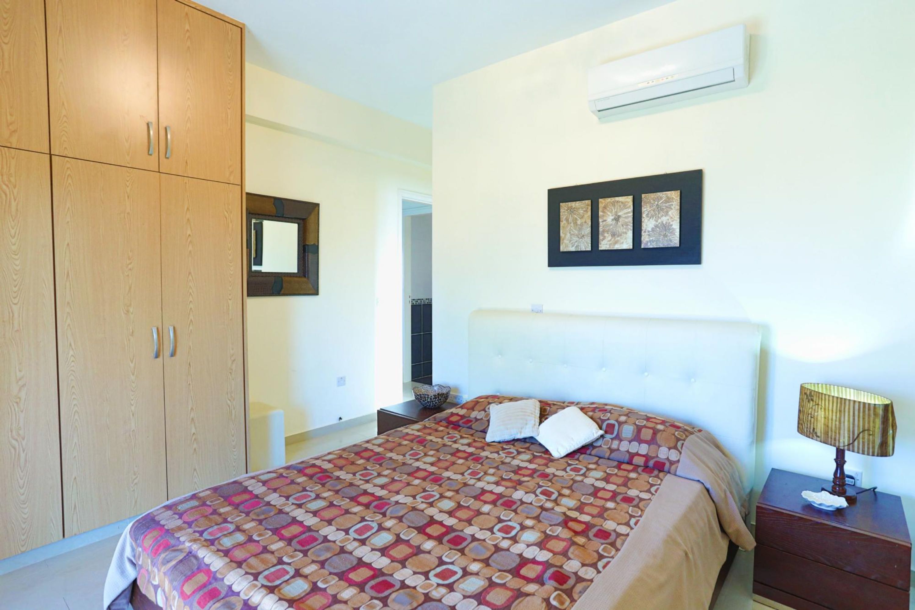Une chambre à coucher avec un grand lit, une armoire, une table de chevet avec une lampe et un climatiseur fixé au mur.