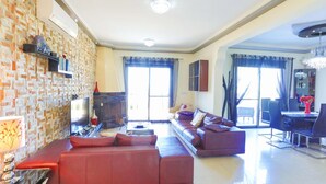 A spacious living room with a red sofa, a flat-screen TV, and a dining area with a chandelier. - Villa Arbanassi in Latchi (Polis)