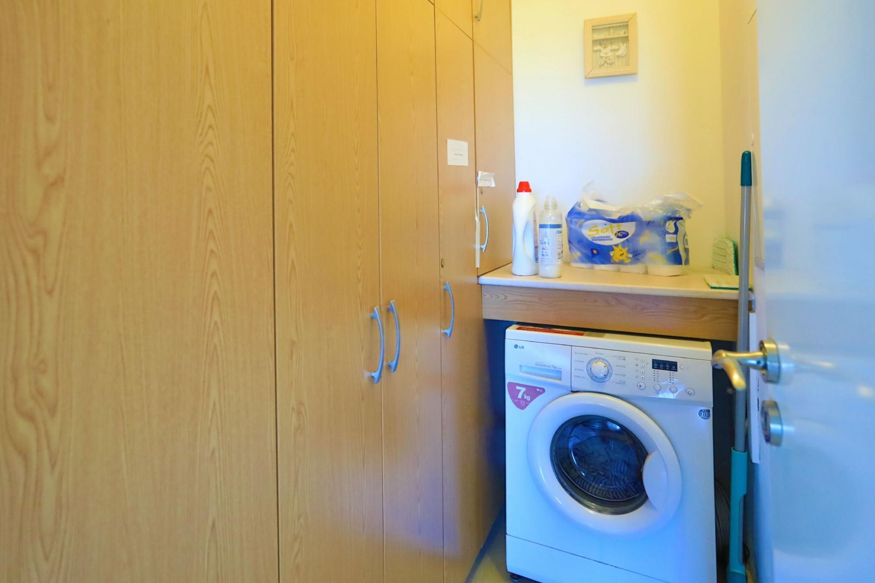 A laundry area with a washing machine, wooden cabinets, and cleaning supplies.