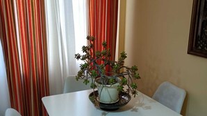 Un coin repas avec une table blanche et quatre chaises blanches. Une plante en pot est posée sur la table.