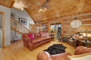 A cozy living room with a brown leather sofa, a wooden ceiling fan, and a large wall clock.