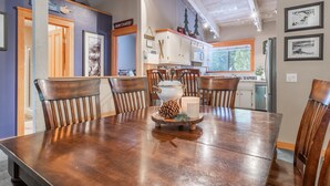 Une salle à manger avec une table et des chaises en bois, une pièce maîtresse décorative et une cuisine en arrière-plan.