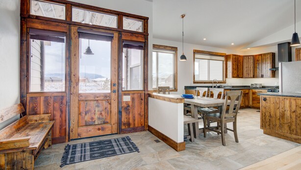 A spacious kitchen with wooden cabinets, a dining area with a bench, and large windows offering a view. - Montana Skies, Livingston, MT! Skiing / Fishing / Yellowstone! (Livingston)