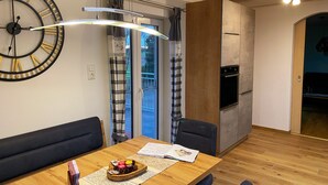 Une cuisine moderne dotée d’un four encastré, d’un coin repas avec une table en bois et d’une grande horloge murale.