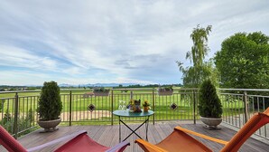 Une terrasse avec deux chaises longues, une table avec une bouteille et des en-cas, et une vue sur un terrain de golf.