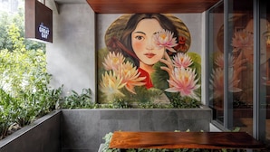 Un interior moderno con un mural de una mujer rodeada de flores, un banco de madera y una zona con bancos de hormigón.