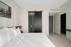 A modern hotel room with a large bed, a sliding door to a bathroom, and a mounted TV.