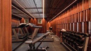 Un gimnasio con cintas de correr, elíptica y un estante con mancuernas.