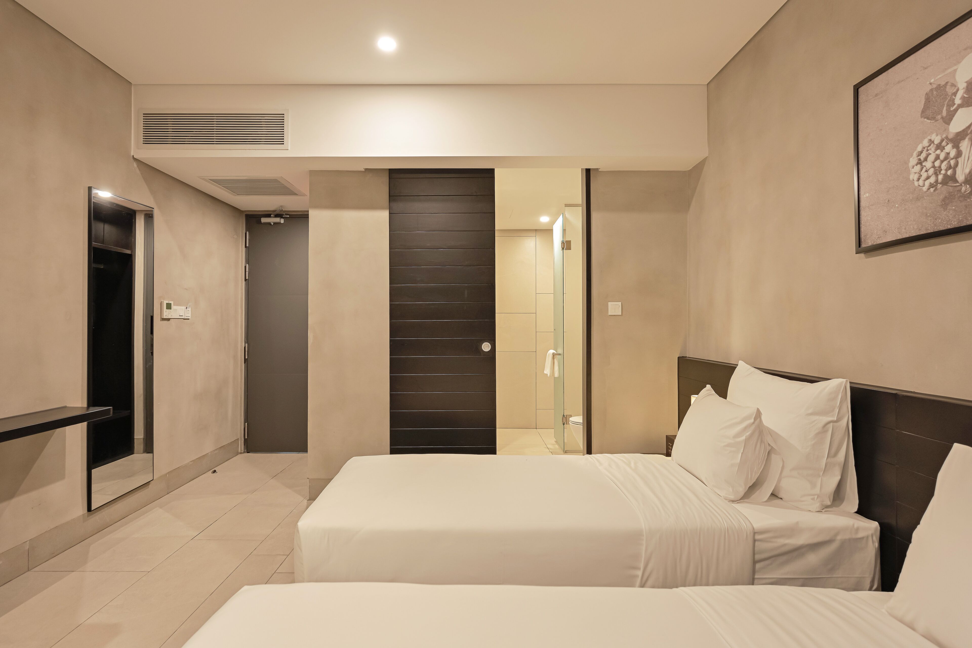 A hotel room with two beds, a dark door, a shower area, and a framed picture on the wall.