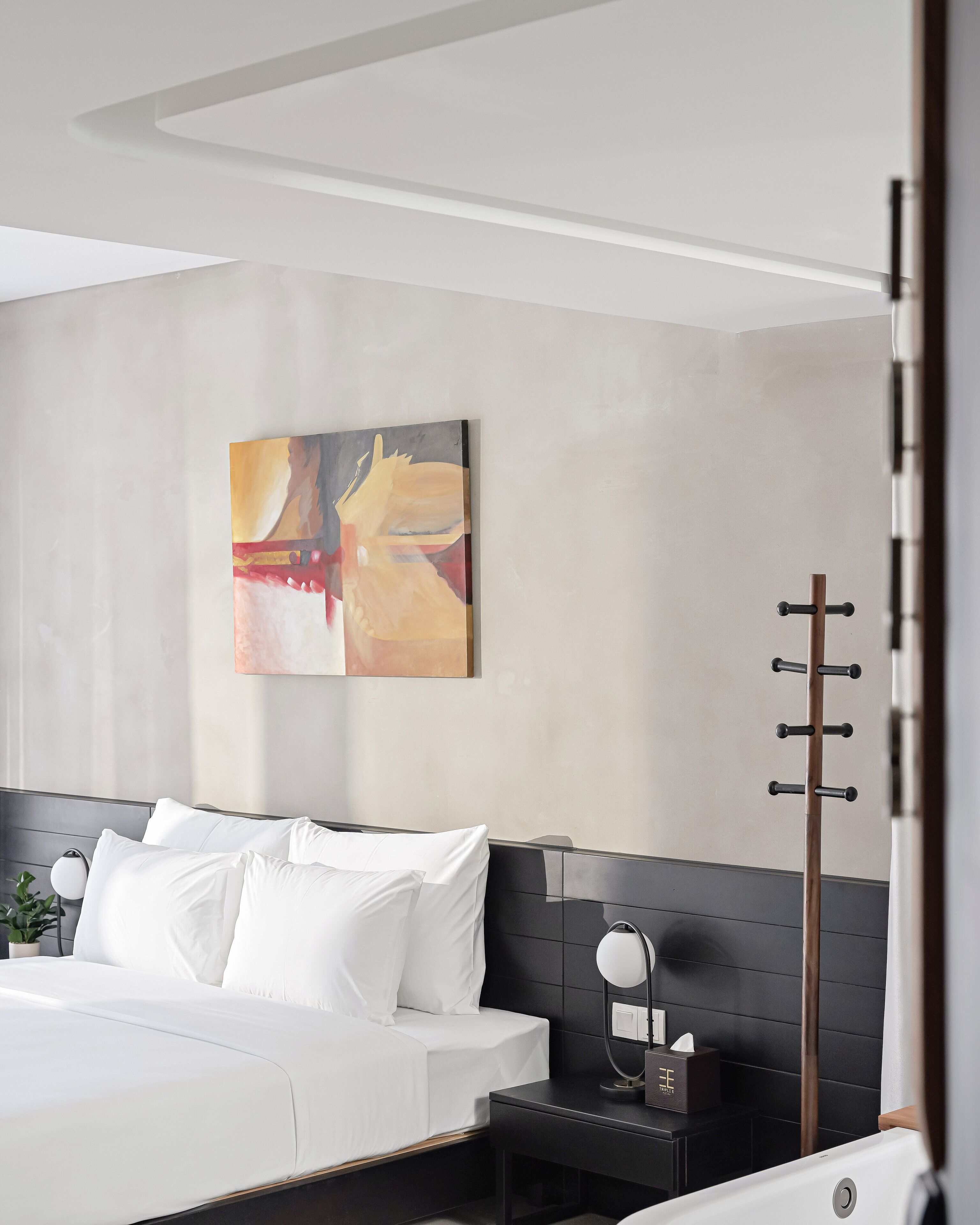 A modern hotel room with a bed, bedside table, and a wall-mounted artwork.