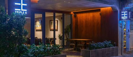 A modern hotel exterior with a prominent "Triple E" sign, large windows, and a covered outdoor seating area.