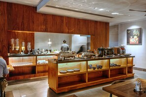 A buffet area with wooden paneling, a counter with various food items, and a person in the background.