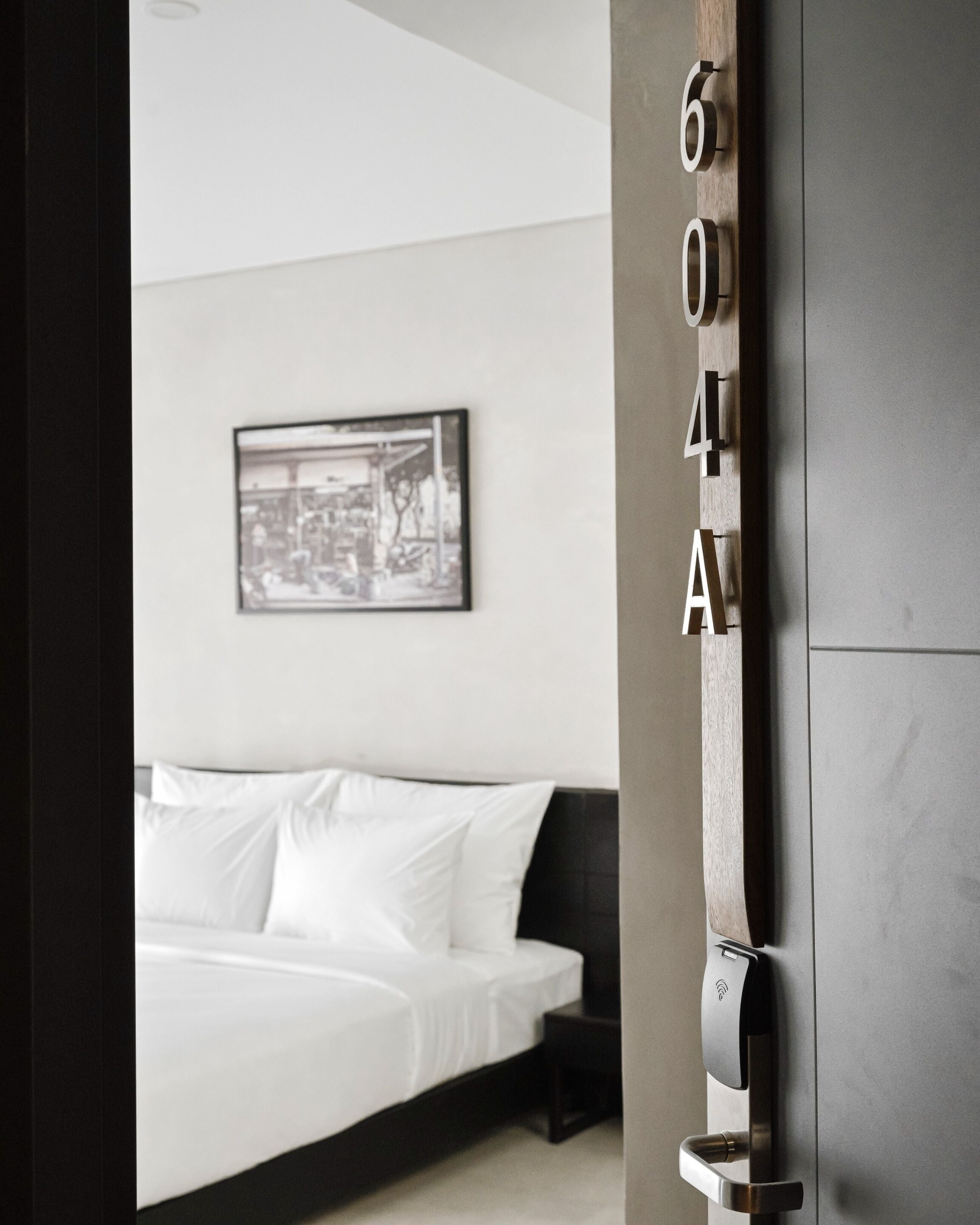 Habitación de hotel con una cama, un cuadro en la pared y una puerta con el número.