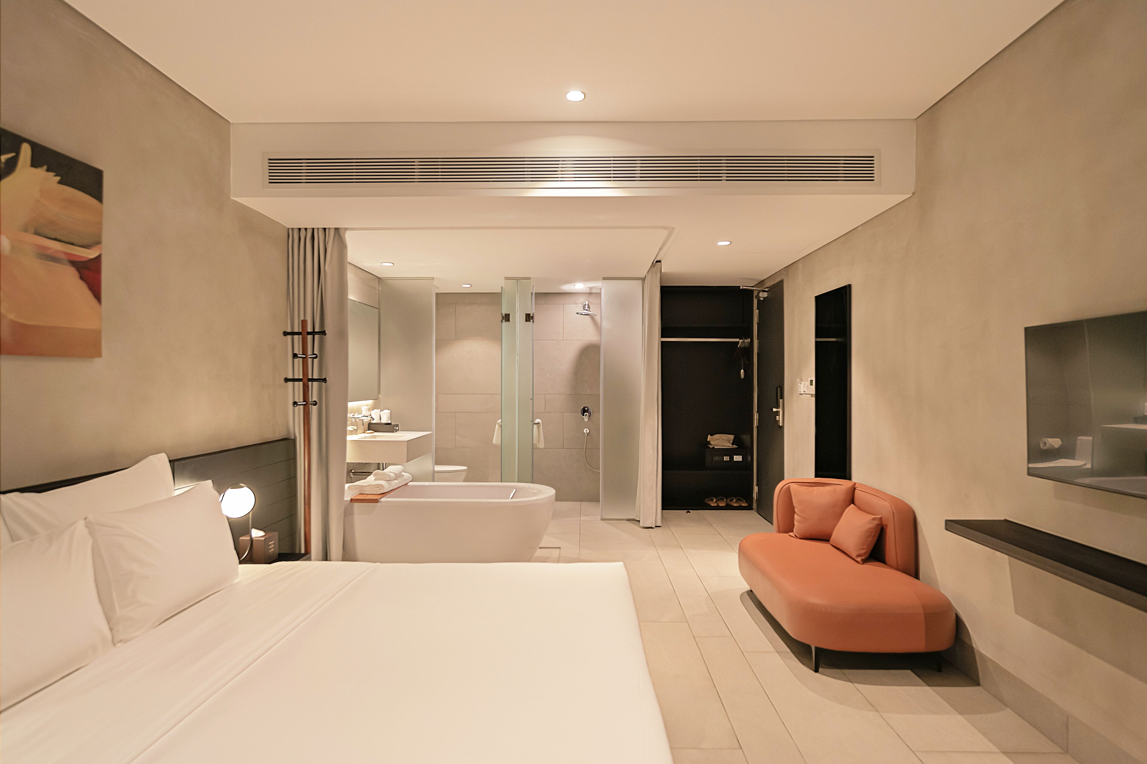A modern hotel room with a large bed, a sitting area, a bathtub, a shower, and a television on the wall.